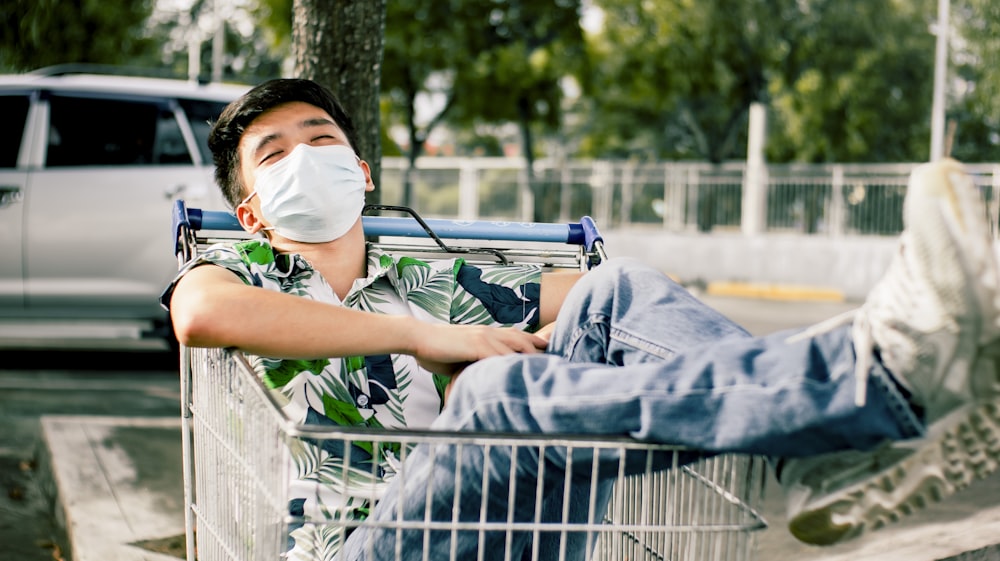a man sitting in a shopping cart wearing a face mask