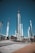 A collection of large, metallic rockets standing upright against a clear blue sky, with some red and black detailing. The area appears to be an outdoor exhibition, with visitors walking around and observing the display. There is a concrete path and platforms surrounding the rockets, and some greenery can be seen in the background.