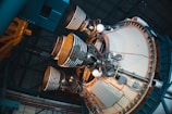 A detailed view of a spacecraft's rocket engines, showcasing several large, cylindrical nozzles partially surrounded by intricate metallic structures and wiring inside a hangar. The engines are mounted on a circular base with visible piping and mechanical components.