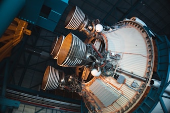 A detailed view of a spacecraft's rocket engines, showcasing several large, cylindrical nozzles partially surrounded by intricate metallic structures and wiring inside a hangar. The engines are mounted on a circular base with visible piping and mechanical components.