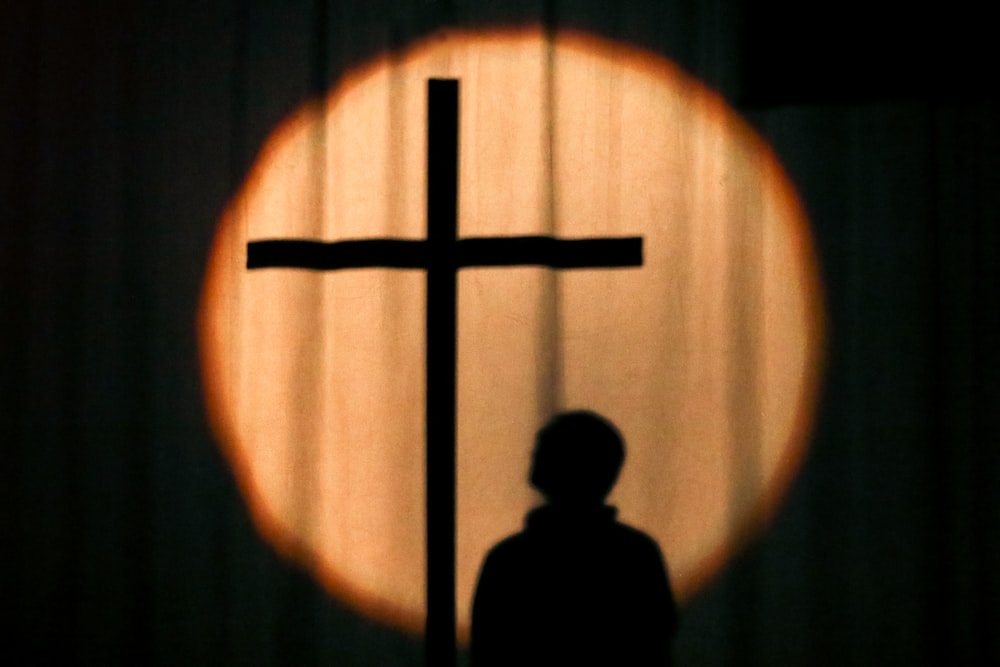 a silhouette of a person standing in front of a cross