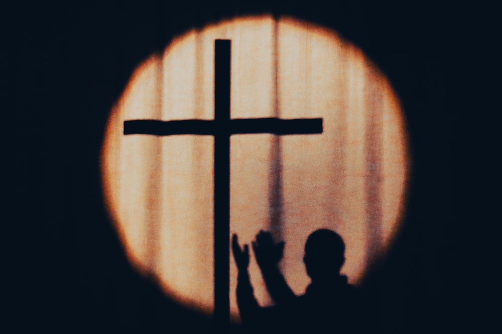a silhouette of a person holding a cross in front of a window