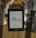A Kindle displaying the title 'O Rei do Inverno' by Bernard Cornwell is placed on a bamboo mat. Surrounding the Kindle are dried leaves, some loose book pages, and black-and-white photographs, creating a vintage and cozy atmosphere.