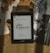 A Kindle displaying the title 'O Rei do Inverno' by Bernard Cornwell is placed on a bamboo mat. Surrounding the Kindle are dried leaves, some loose book pages, and black-and-white photographs, creating a vintage and cozy atmosphere.