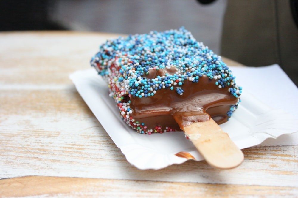 a chocolate covered ice cream with sprinkles on a white plate