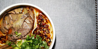 A vibrant bowl of hand-pulled beef noodles garnished with fresh herbs and chili oil.
