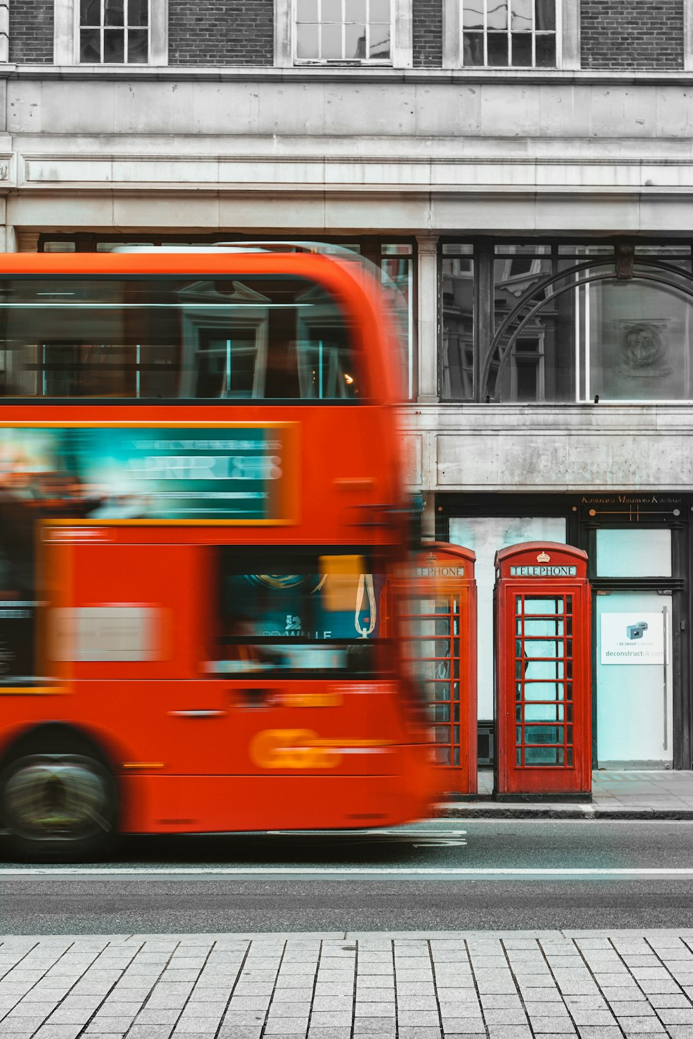 a red double decker bus driving past a tall building