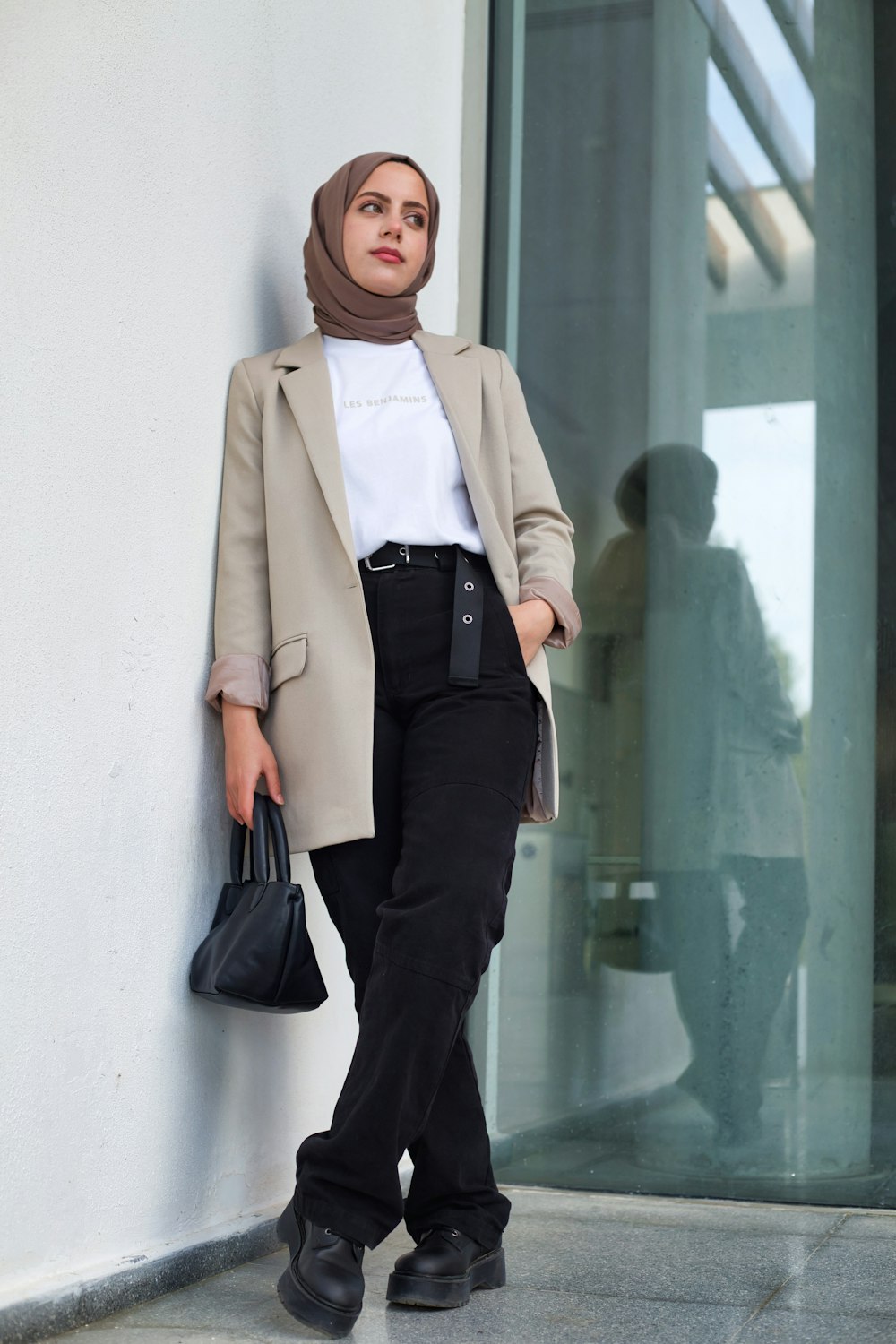 a woman leaning against a wall holding a purse