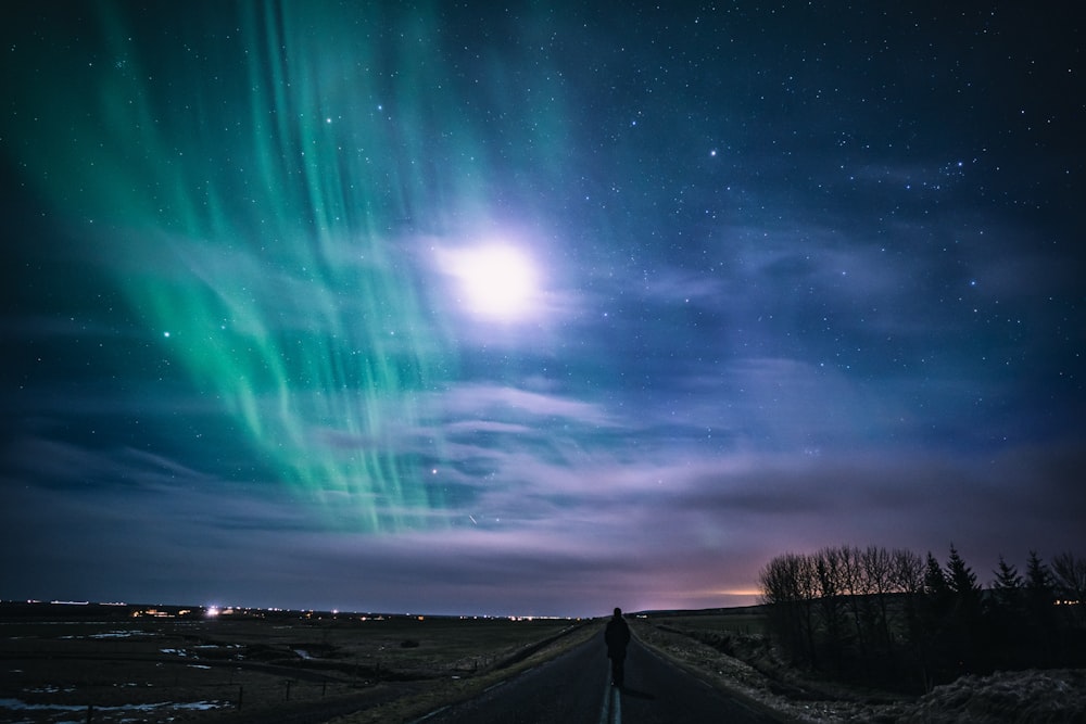 a person standing on the side of a road under a night sky