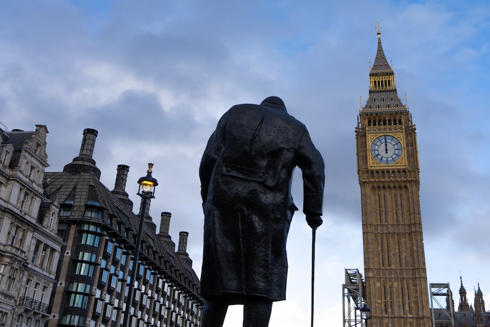 Una statua di un uomo in piedi accanto a una torre dell'orologio