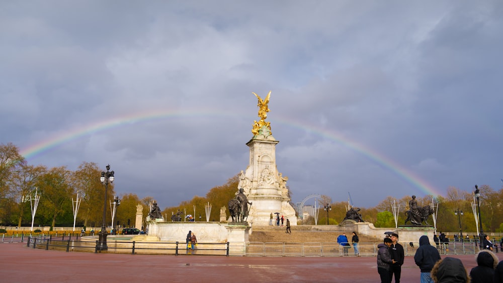 a group of people standing around a statue with a rainbow in the background