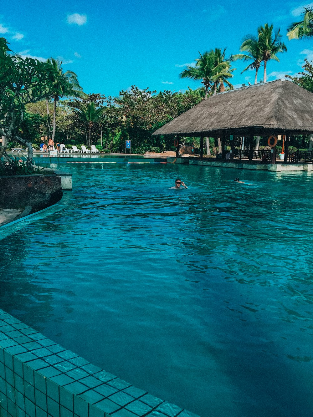 a person swimming in a pool with a hut in the background