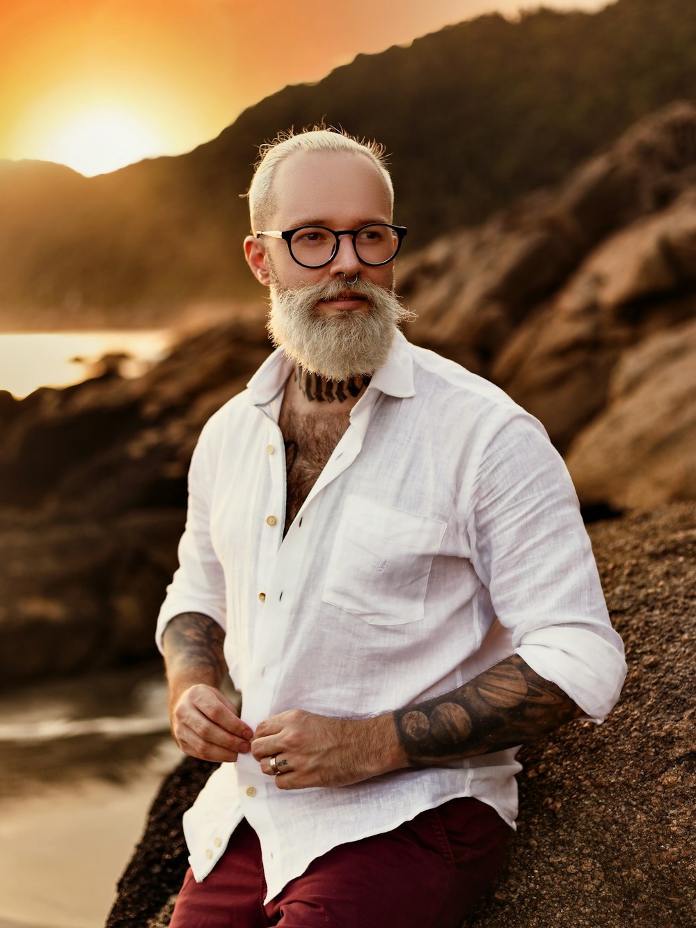 a man with a beard and glasses sitting on a rock