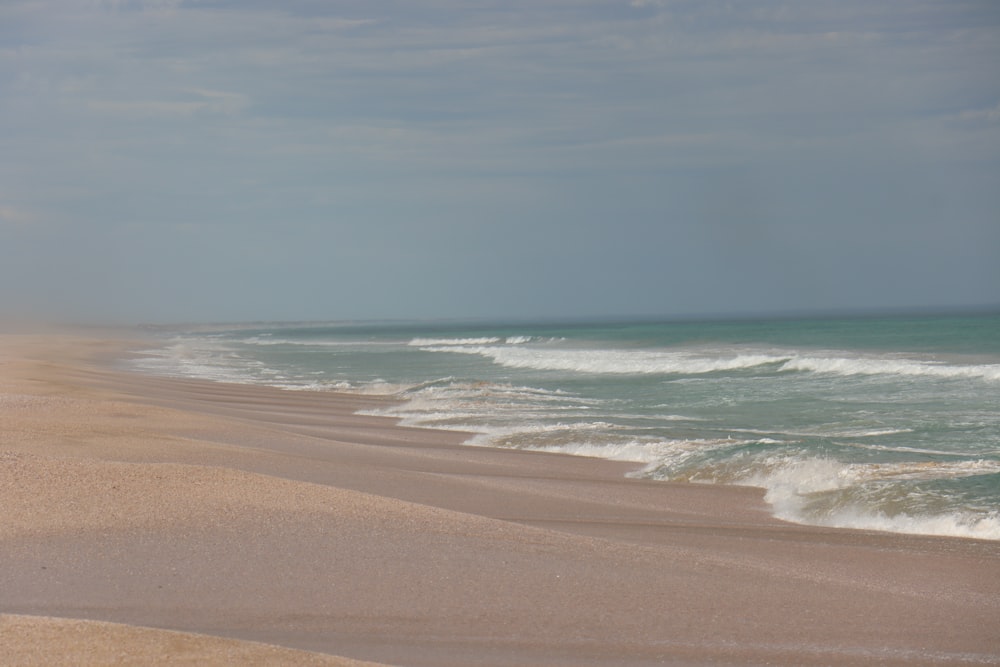 a sandy beach next to the ocean under a cloudy sky