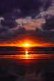 the sun is setting over the ocean on a cloudy day