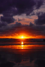 the sun is setting over the ocean on a cloudy day