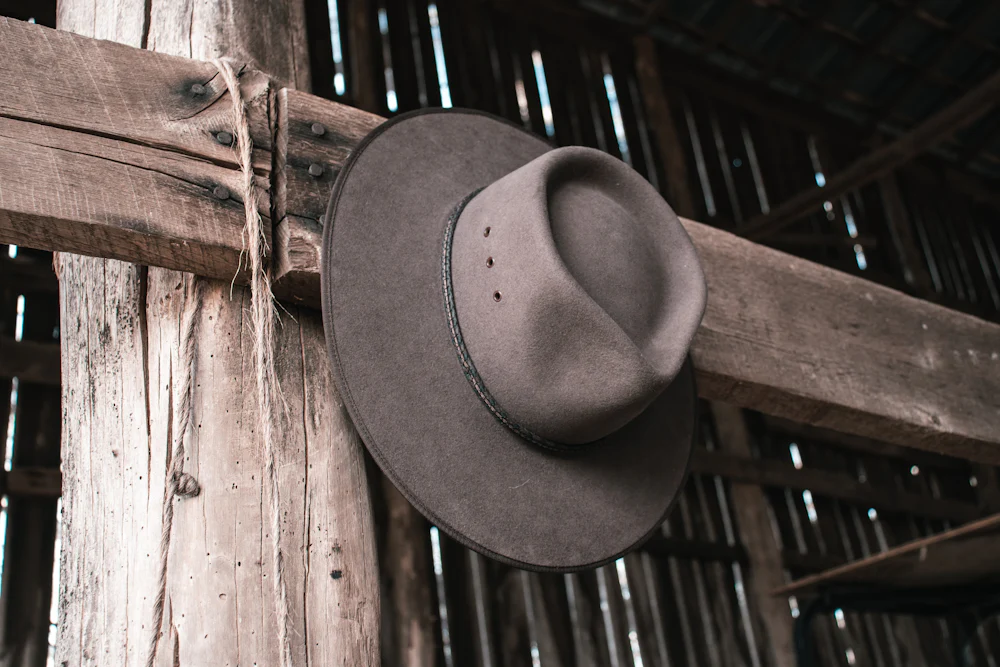 A grey felt hat hanging on a timber beam inside a barn.