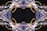 An intricate, symmetrical abstract pattern resembling a kaleidoscope, featuring swirling colors and shapes that appear fluid and dynamic. The design is centralized with elaborate loops and delicate lace-like details, blending hues of blue, purple, white, and gold.