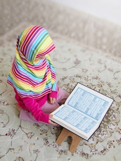 a little girl sitting on a stool reading a book