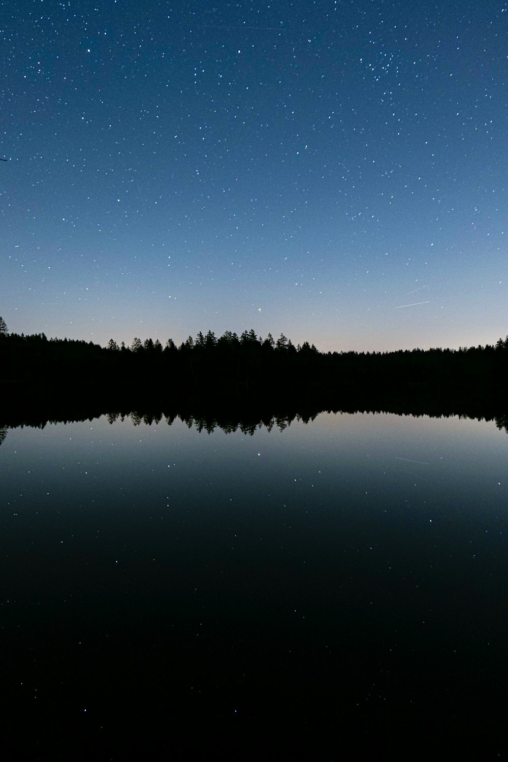 the night sky is reflected in the still water of a lake