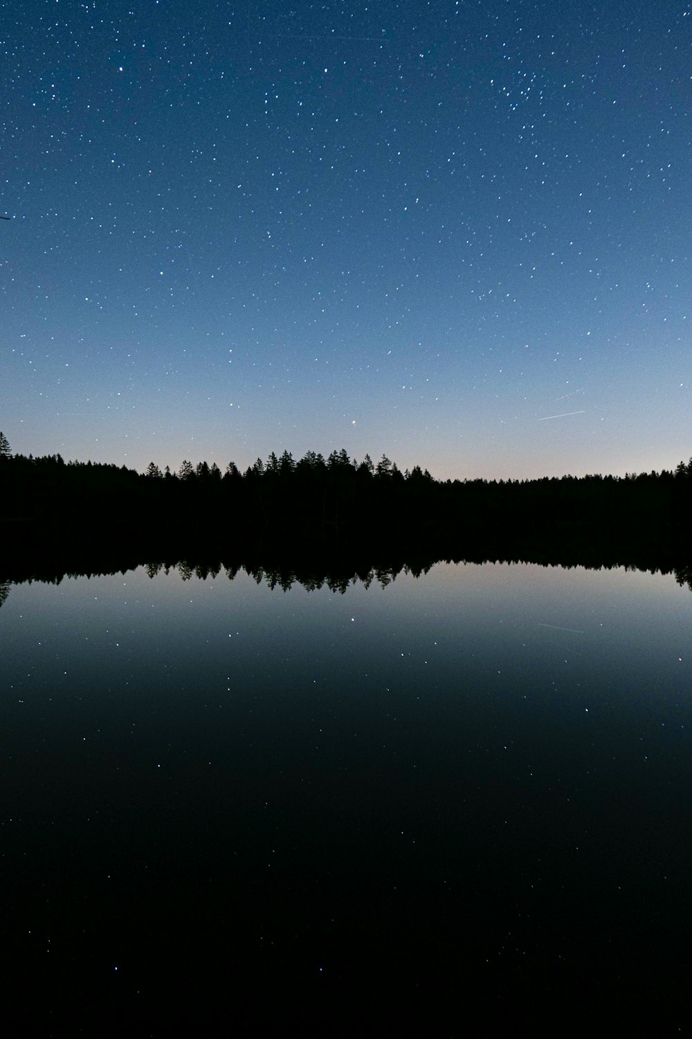 El cielo nocturno se refleja en el agua quieta de un lago