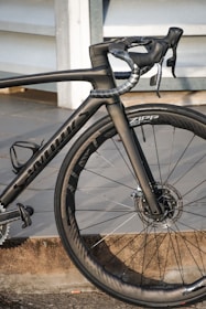 A high-performance road bicycle with a sleek black frame and aerodynamic design, featuring carbon fiber components and disc brakes. The bike is equipped with Zipp wheels, showcasing precision engineering and attention to detail.
