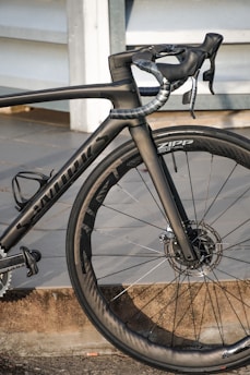 A high-performance road bicycle with a sleek black frame and aerodynamic design, featuring carbon fiber components and disc brakes. The bike is equipped with Zipp wheels, showcasing precision engineering and attention to detail.