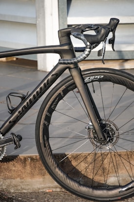 A high-performance road bicycle with a sleek black frame and aerodynamic design, featuring carbon fiber components and disc brakes. The bike is equipped with Zipp wheels, showcasing precision engineering and attention to detail.