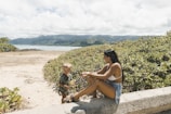 a woman sitting next to a little boy on a beach