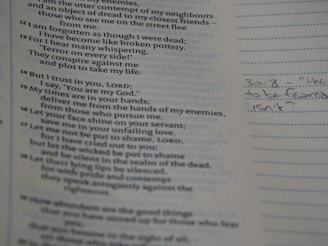 The image features a close-up view of a page from a book with printed text and handwritten notes in the margins. The printed content appears to be poetic or biblical in style, with numbered verses. On the right, there is a handwritten note in pencil, possibly reflecting on the text.