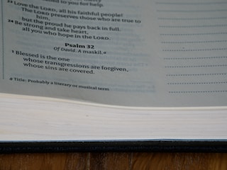A page from the Bible displaying text from Psalm 32, with a focus on the verse highlighting forgiveness. The page is part of a book with a visible spine and margins, displayed under natural lighting.