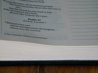 A page from the Bible displaying text from Psalm 32, with a focus on the verse highlighting forgiveness. The page is part of a book with a visible spine and margins, displayed under natural lighting.