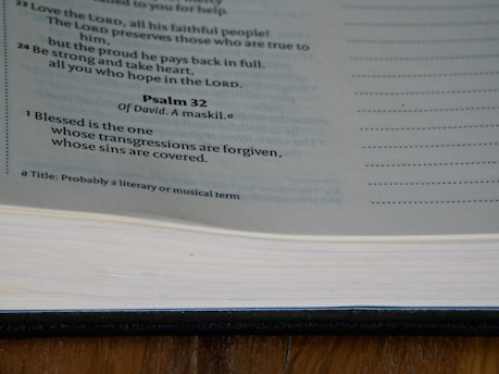 A page from the Bible displaying text from Psalm 32, with a focus on the verse highlighting forgiveness. The page is part of a book with a visible spine and margins, displayed under natural lighting.