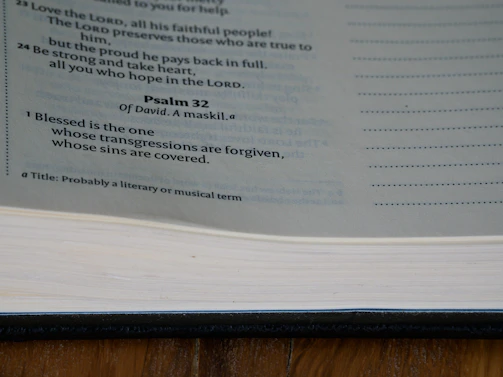 A page from the Bible displaying text from Psalm 32, with a focus on the verse highlighting forgiveness. The page is part of a book with a visible spine and margins, displayed under natural lighting.