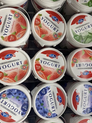 Several tubs of Swiss Premium Yogurt are displayed. The flavors visible include strawberry, aloe vera, and blueberry. The labels indicate that the yogurt is low-fat and made in Switzerland, with images of the corresponding fruits on each tub.