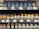 Shelves stocked with various brands of honey jars and bottles, including products labeled as organic and manuka blend from different countries such as New Zealand and Belgium. The display includes a range of container types, including glass jars and plastic squeeze bottles.