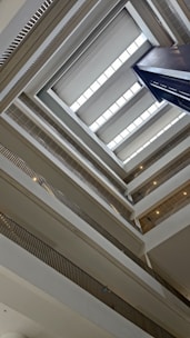 The image captures the interior view of a multi-story building, showcasing an architectural perspective looking up. The shot reveals multiple levels with a series of balconies and railings lining the open central space. Natural light enters through rectangular skylights positioned near the ceiling.