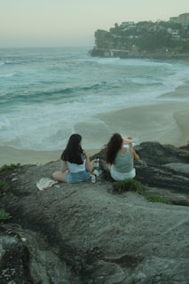 two women sitting on a rock overlooking the ocean
