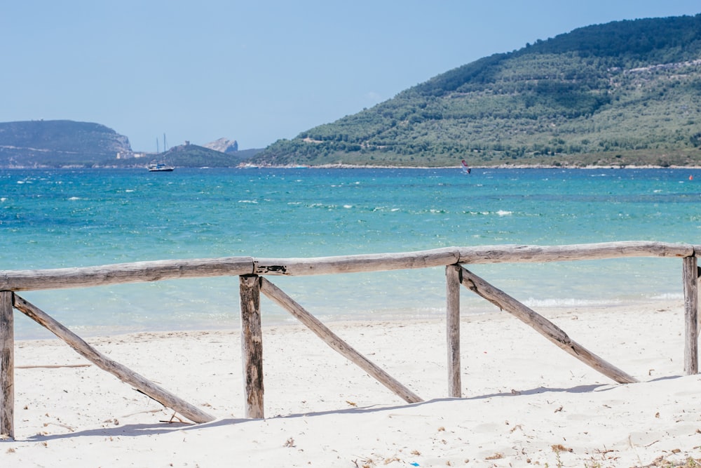 a wooden fence on a beach with a body of water in the background