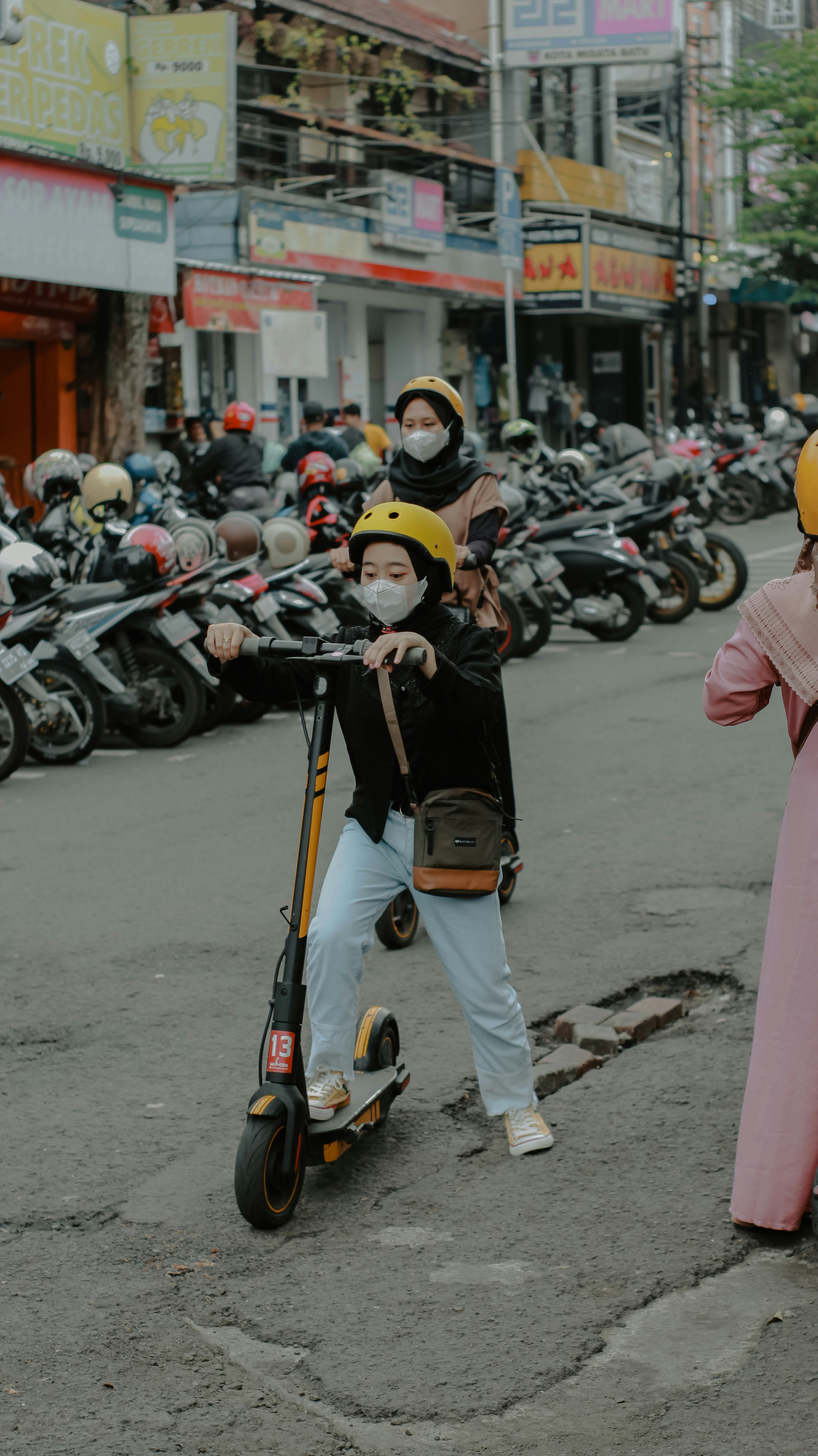 A woman standing next to a child on a scooter
