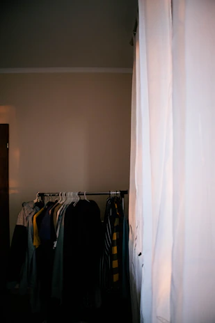 A cozy, sunlit studio with a selection of men's jackets and shirts neatly displayed on wooden hangers.