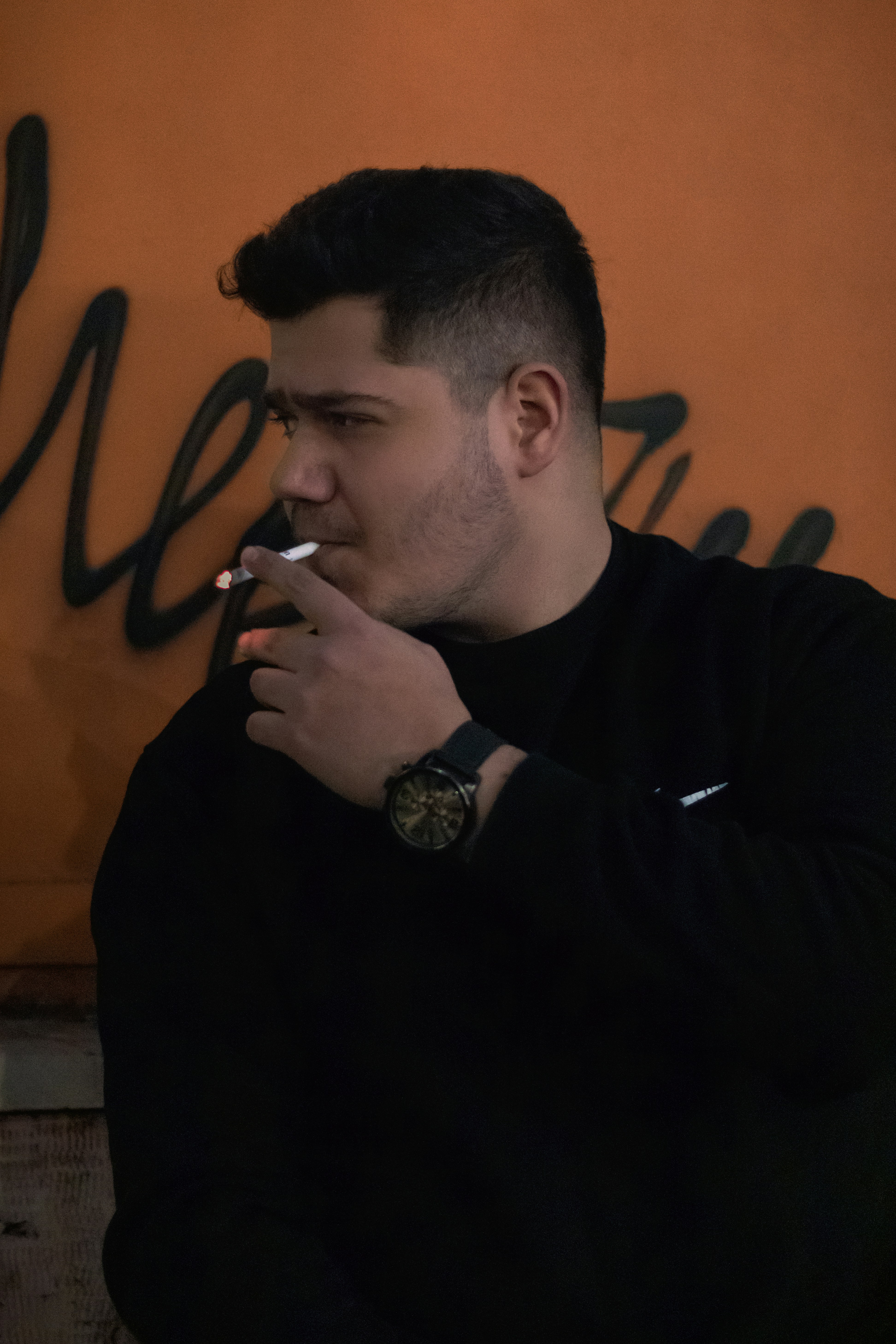 a man smoking a cigarette in front of a wall