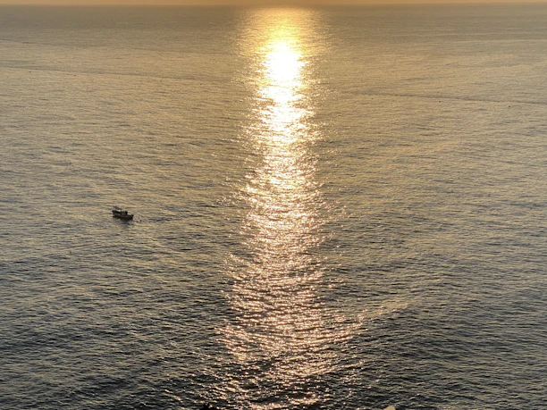 Wide-angle view of a boat cutting through golden hour waters under an open horizon sky.