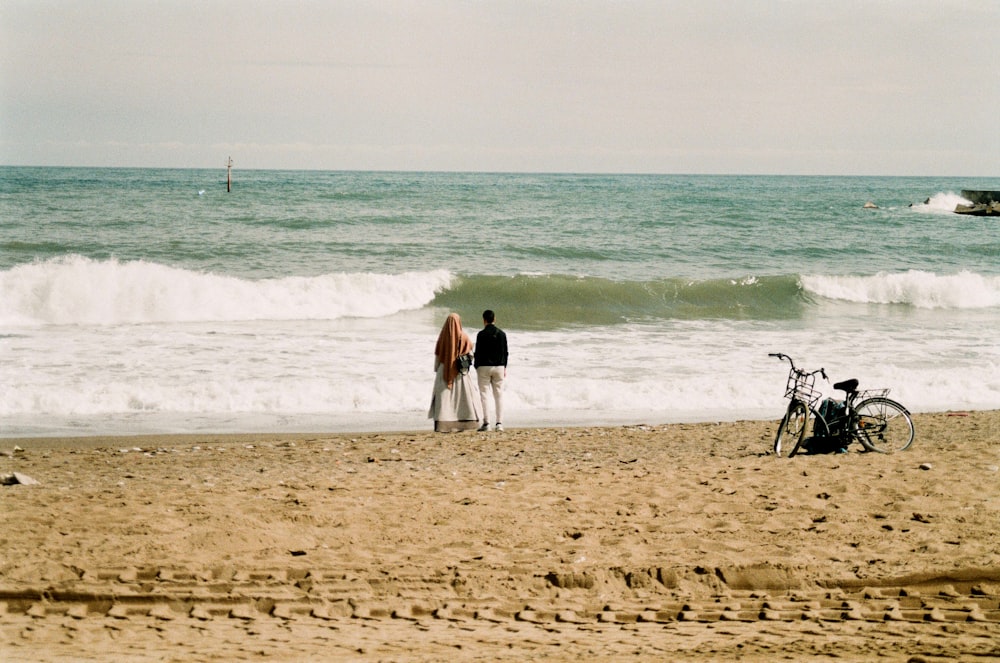 a couple of people standing on top of a sandy beach