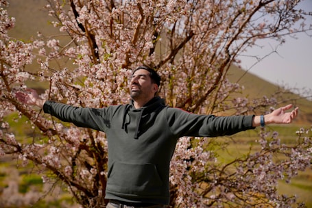 A person sneezing outdoors surrounded by blooming trees, illustrating hay fever.