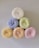 Six rolls of yarn arranged in a pyramid formation, featuring a variety of colors including white with speckles, blue, green, yellow, orange, and pink. The texture appears soft and fluffy, suggesting the yarns are made of a fine, delicate material.