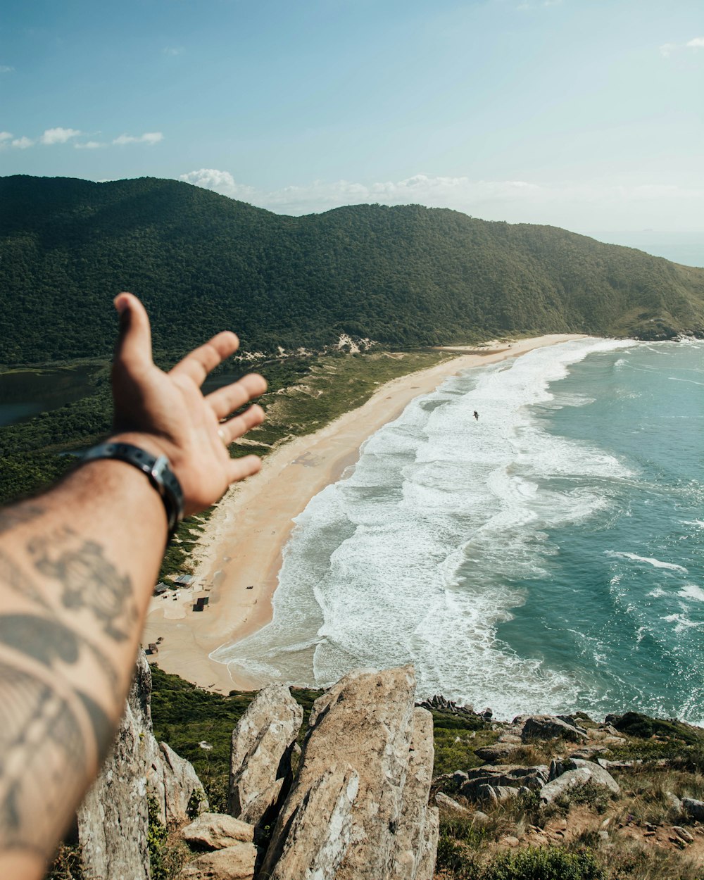 a person's hand reaching out towards the ocean