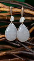 Delicate clay earrings inspired by nature, hanging from a rustic wooden branch.