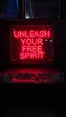 A red neon sign with the words 'Unleash Your Free Spirit' is prominently displayed above a dimly lit area, possibly a showcase or display. The bright neon contrasts with the dark background, creating a striking visual effect.