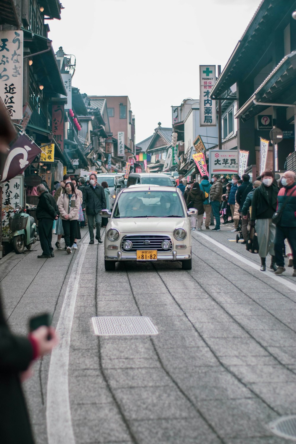 Un pequeño automóvil conduciendo por una calle junto a una multitud de personas